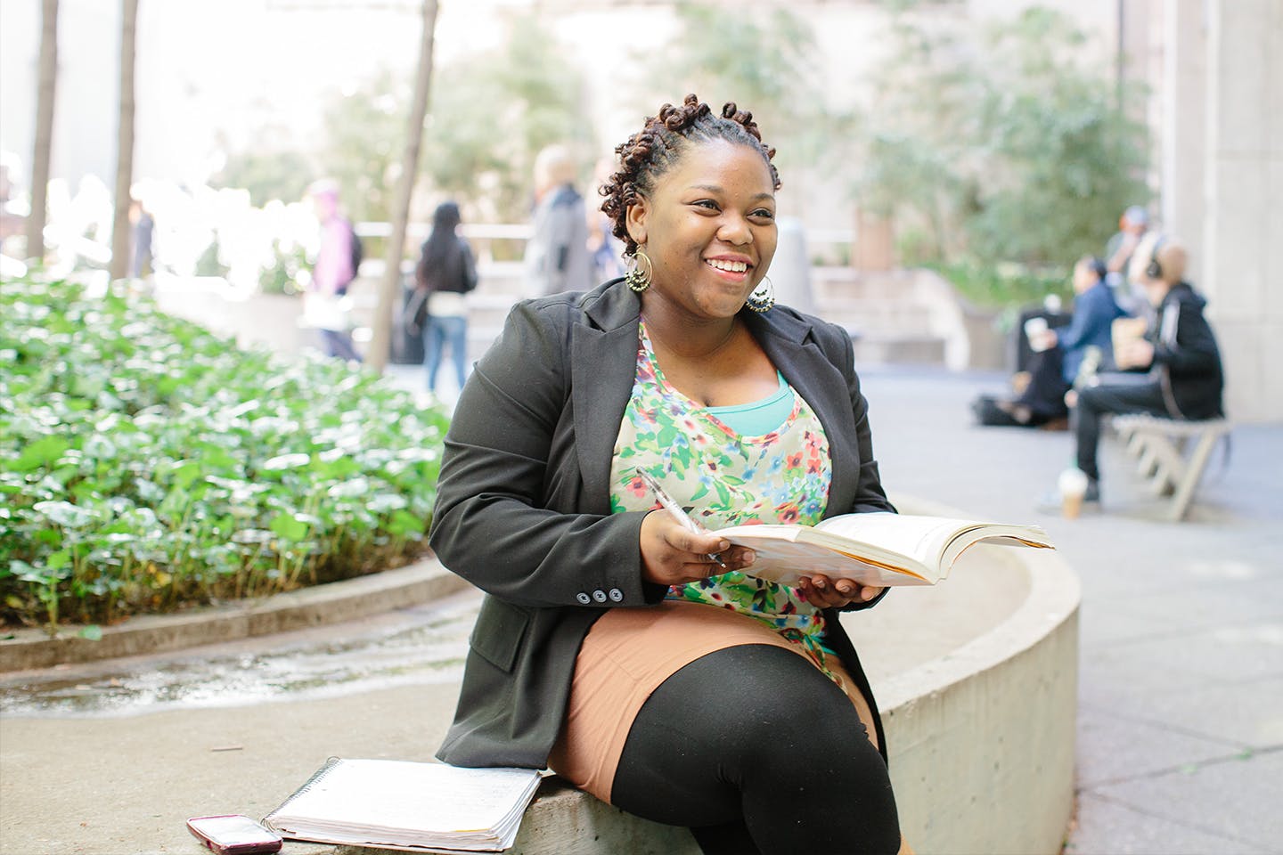 New School student sitting by fountain holding a book smiling